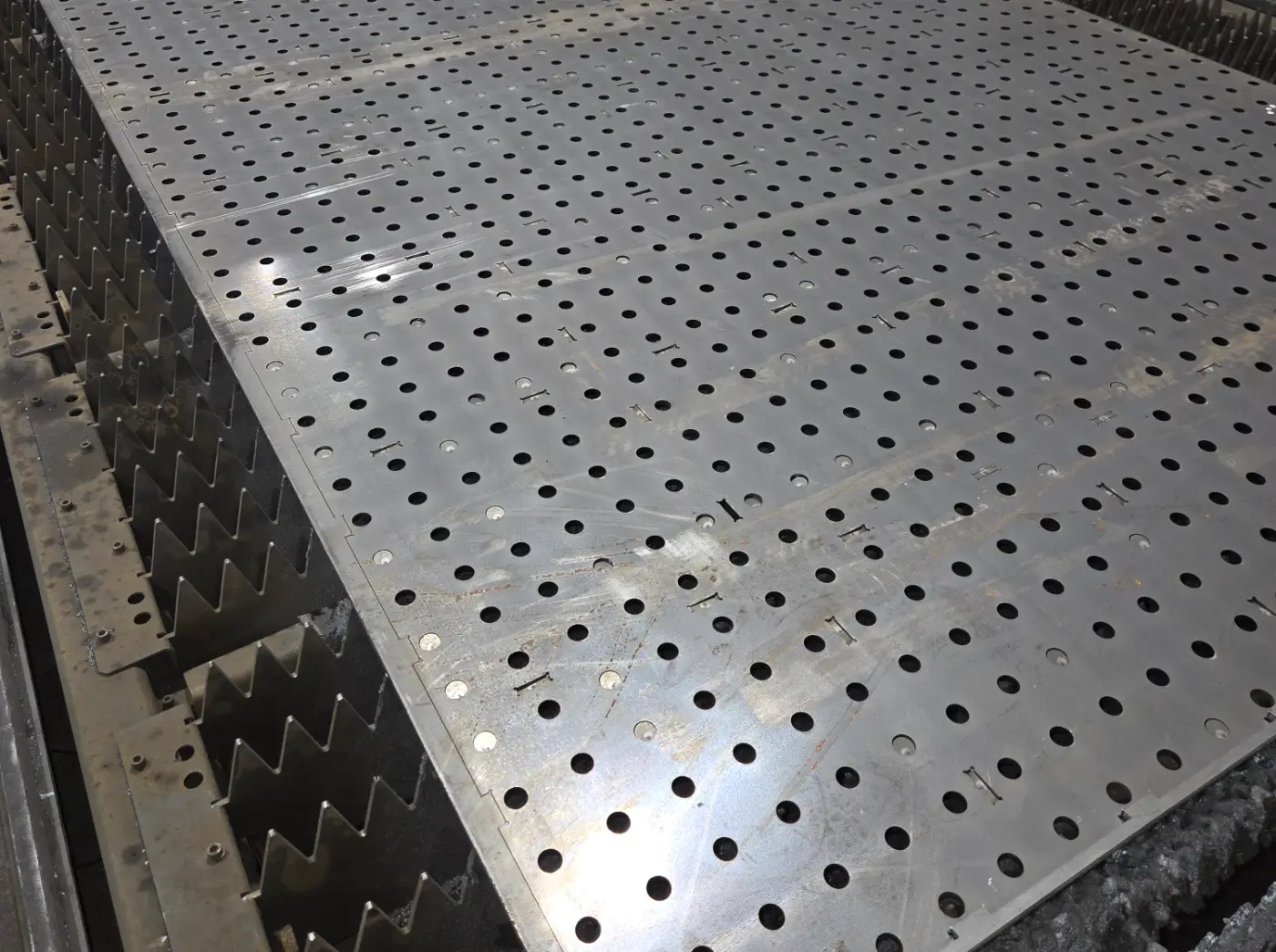 Full steel sheet on a laser table after cutting, with rows of holes and part outlines